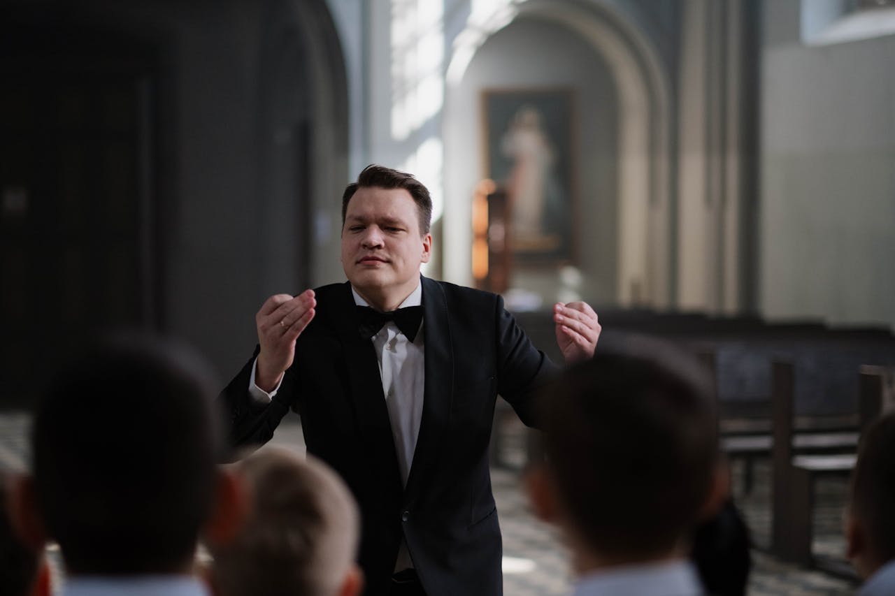 A male conductor leads a boys choir rehearsal in a serene church setting.