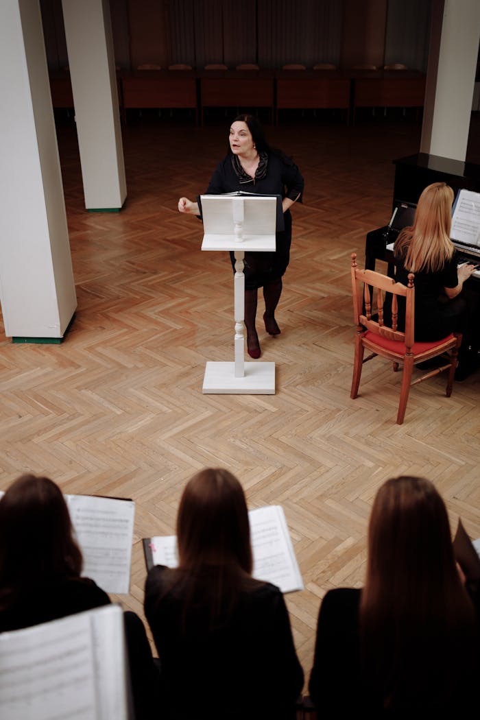 Conductor leading choir practice in a spacious room with piano accompaniment.